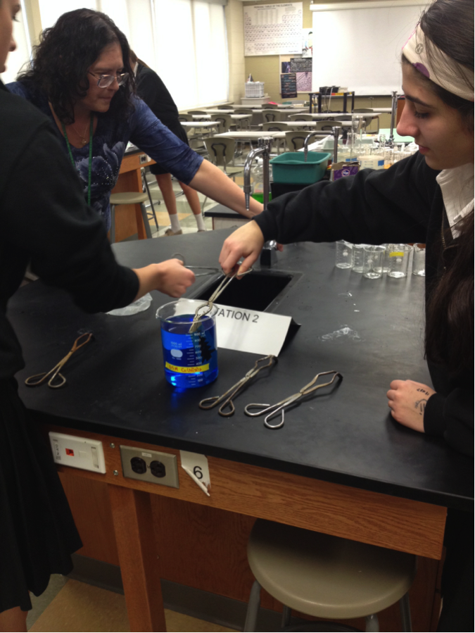 Students dip metal ornaments into chemicals to reveal designs.