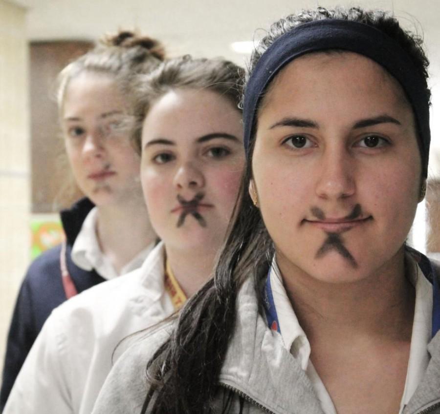 Mercy students (from left) freshman Kaylie Scott, junior Megan McCarren, and senior Natalie Cieslak stand out from the crowd with a black X for silence. (Photo illustration: Caitlin Somerville)