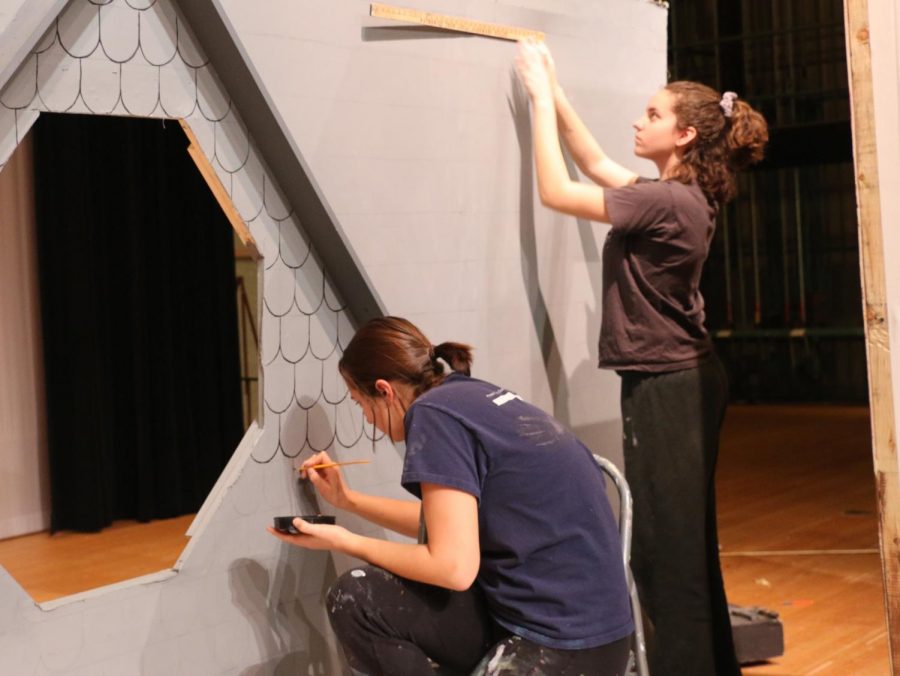 Senior Abbey Hembree paints individuals shingles on the rooftop while other members of Stage Crew build and paint other parts of the set.