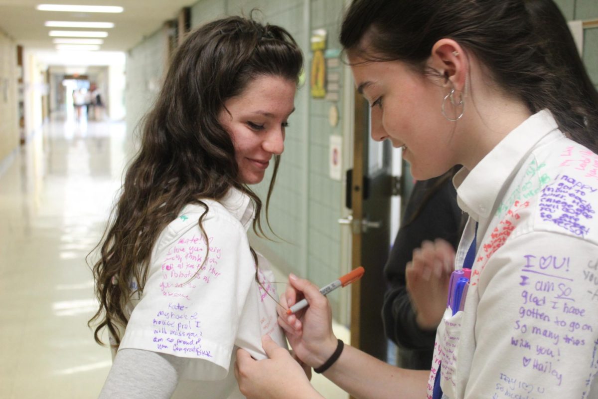 Senior signs another seniors shirt with a kind message.